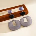 Detail view of purple and grey acrylic geometric earrings on a wooden stand. - Gray
