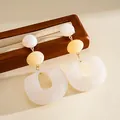 Macro view of white marble pattern acrylic geometric drop earrings on wooden stand - White