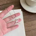 Detailed view of a hand holding a minimalist silver starfish pendant necklace on a thin chain - Seastar Pendant Style / Silver