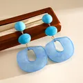 Close-up detail showing the textures of blue acrylic geometric earrings on a wooden stand - Blue