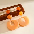 Detail view of orange acrylic geometric earrings with layered beads and oval drop. - Brown