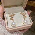 Primer plano de pendientes dorados de hoja de ginkgo con perlas y circonitas en caja rosa - Dorado