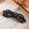 Gros plan d'une barrette à nœud en tissu floral noir sur un plateau à bijoux en velours beige - Pince Torsadée - Noir et Blanc Floral