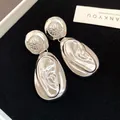 Close-up of silver-toned drop earrings with artistic wrinkled texture and metallic finish - Silver