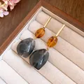 Macro detail of geometric resin drop earrings with amber and grey marble texture in a jewelry box. - Coffee-Black