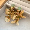 Close-up of gold filigree flower petal earrings with speckled green stone tassels in a box. - Gold-Green