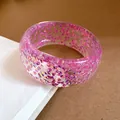 Primo piano di un bracciale rigido in resina trasparente con glitter viola iridescenti. - Viola