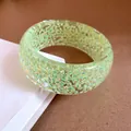 Primo piano di un bracciale in resina verde iridescente con glitter e finitura lucida. - Verde