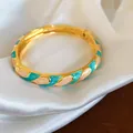 Vue détaillée d'un jonc doré élégant avec des motifs de pétales en émail bleu et pêche - Or, Blanc et Cyan