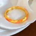 Gros plan d'un jonc plaqué or avec motifs en émail orange et jaune sur de la soie blanche - Or, Jaune et Orange