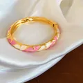 Vue détaillée d'un jonc émaillé doré avec des motifs floraux roses et blancs - Or-Blanc-Rose