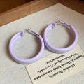 Detail view of light purple spray-painted hoop earrings on a textured background - Large / Purple