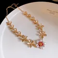 Dettaglio di una collana in metallo dorato con un ciondolo a forma di fiore in smalto bianco - Collana / Oro-Rosso
