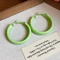 Detailed view of minimalist light green lacquered hoop earrings on textured fabric - Large / Green