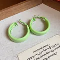 Close-up detail of light green spray-painted hoop earrings on a fine linen texture. - Small / Green