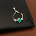 Gros plan d'une bague chaîne ajustable avec zircon vert et perle coulissante. - Bague Chaîne Réglable / Ton Argent Avec Pierre Verte