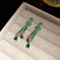 Close-up of silver teardrop earrings with emerald green crystals in a gray jewelry box - Green