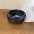 Close-up view of a thick black resin bangle featuring colorful iridescent glitter flakes - Black