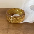 Detailed macro shot of a chunky amber resin bangle with sparkling gold glitter and stars. - Brown