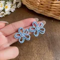 Primo piano di orecchini a fiore blu traforati con perle centrali, gioielli chic - Blu