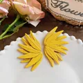 Close-up of vibrant yellow leaf-textured stud earrings displayed on a white beaded plate - Yellow