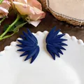 Detailed view of blue leaf-textured statement earrings on a white decorative plate. - Blue and Purple