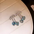 Close-up of bow knot earrings with sparkling blue heart crystal tassels on a beige tray. - Iridescent Blue