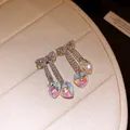 Close-up of iridescent heart drop earrings with bowknot crystal accents - White