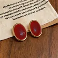 Primo piano di eleganti orecchini vintage ovali in resina rossa con bordi dorati. - Oro-Rosso