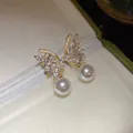 Close-up of elegant butterfly earrings with sparkling zircons and dangling pearls - Butterfly Pearl Stud Earrings (HE33176) / Gold