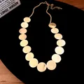 Detailed view of a golden necklace featuring multiple brushed metal circular discs. - Necklace - Gold