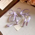 Dettaglio di eleganti orecchini a fiocco in raso lavanda su sfondo rustico estetico. - Viola