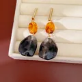 Primer plano de pendientes de resina vintage con motivos de ámbar y humo en un joyero. - Café-Negro