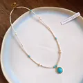 Close-up of vintage beaded necklace with a circular turquoise stone pendant on a white plate - Turquoise Pendant / Gold-White-Blue