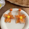 Close-up of orange mesh flower earrings with raffia woven detail for a summer beach look - Simulated 3D Flower Style / Orange