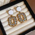 Close-up of vintage gold-tone earrings with white circular studs and blue crystal frames - White Drop
