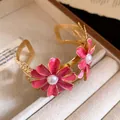 Detailed view of gold-toned pink enamel flower bangle with pearls in a jewelry tray. - Pink