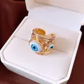 Close-up of a gold-colored evil eye open ring with blue resin details in a gift box. - Open Ring / Gold