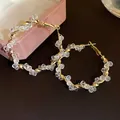 Detailed view of twisted gold-tone hoop earrings with sparkling clear crystal beads. - Twisted Style / Gold-White