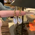 Dettaglio di orecchini huggie dorati in stile francese con pendenti a goccia d'acqua. - Oro + Argento