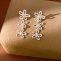 Close-up of elegant silver hollow flower drop earrings on a brown velvet stand. - Triple Hollow Flower Style / Silver