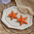 Macro view of vibrant orange enamel starfish earrings perfect for beach vacations. - Orange