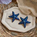 Detailed view of blue enamel starfish earrings with gold trim and pearl center - Blue