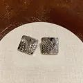 Dettaglio di orecchini a lobo quadrati color argento con elegante trama a rombi fini - Argento