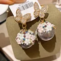 Dettaglio ravvicinato di eleganti orecchini a farfalla con perle e micro fiori. - Oro + Multicolore