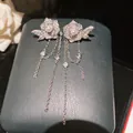 Primo piano di orecchini a rosa in argento con zirconi, perla e lunghe nappe a catena - Argento