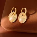 Dettaglio macro di orecchini pendenti vintage dorati con perla e motivo a stella in zircone. - Oro