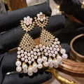 Primo piano di orecchini a pendaglio dorati con perle bianche e zirconi lucenti. - Oro+Bianco