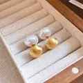 Primo piano elegante di orecchini a perno in oro spazzolato e perle in un portagioie di legno - Oro con Bianco