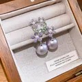 Dettaglio di orecchini floreali con zirconi e perle lavanda in una scatola di legno - Argento + Porpora